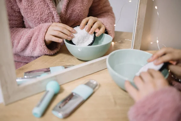 Girls hands putting cotton pad in a bowl with a lotion