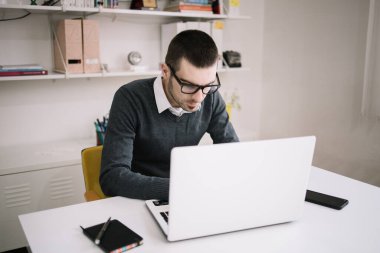 Masasında dizüstü bilgisayar kullanan gözlüklü bir ofis çalışanı.