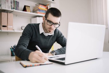 Ofis çalışanı masada oturuyor ve deftere yazıyor.
