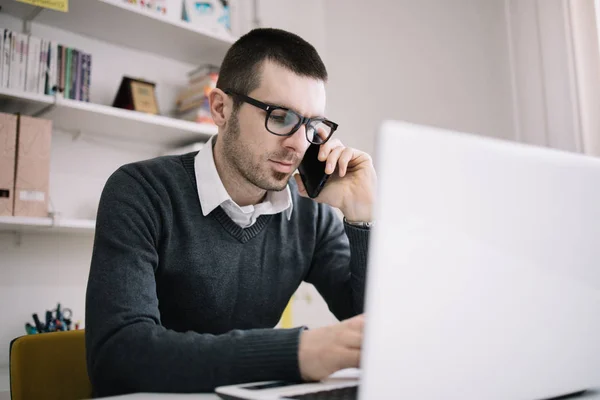 Man with glasses using phone while sitting at office desk