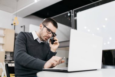 Erkek işçi telefonla konuşuyor ve dizüstü bilgisayara bakıyor.