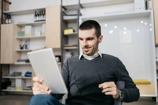 Hombre feliz sentado y sosteniendo una tableta — Foto de Stock