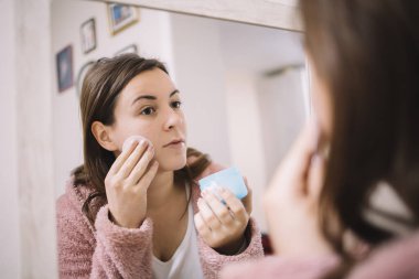 Pembe bornozlu kadın cildini pedlerle fırçalıyor.