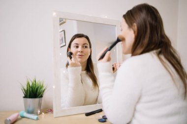 Güzel kız fırçayla allık sürüyor ve aynaya bakıyor.