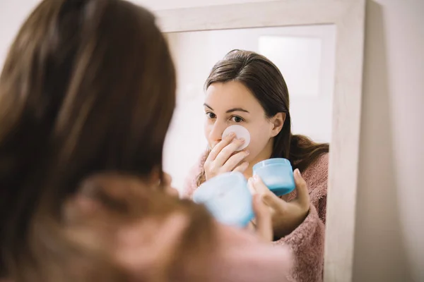 Chica aplicando crema en su cara delante del espejo — Foto de Stock