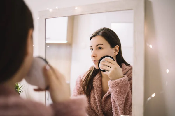 Mujer mirando el espejo aplicando polvo a su cara — Foto de Stock