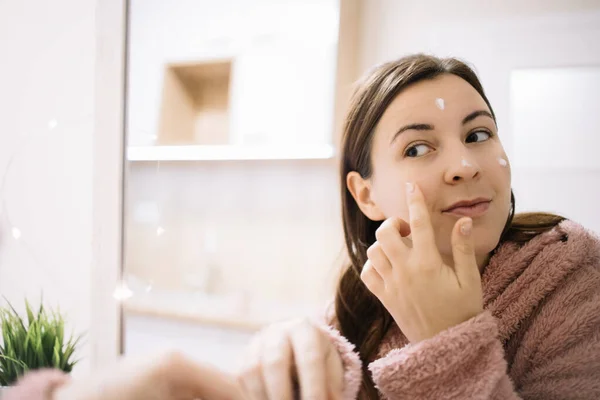 Imagen reflejada de la mujer aplicando crema facial — Foto de Stock