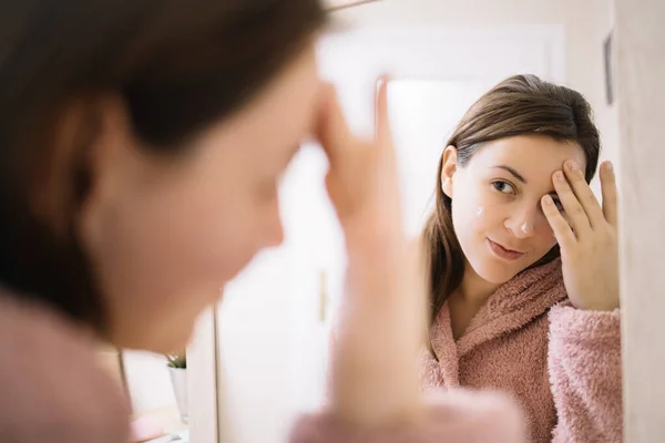 Reflejo de una mujer con bata rosa aplicando mascarilla facial — Foto de Stock