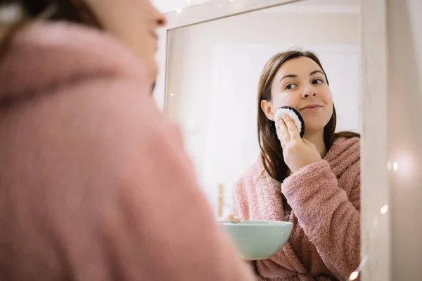 Mujer joven aplicando tratamiento facial frente al espejo — Foto de Stock