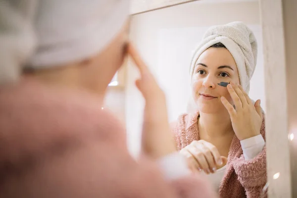Reflejo del espejo de una chica que se aplica una máscara de barro en la cara — Foto de Stock