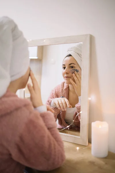 Reflejo de una chica frotando crema de barro en su cara — Foto de Stock