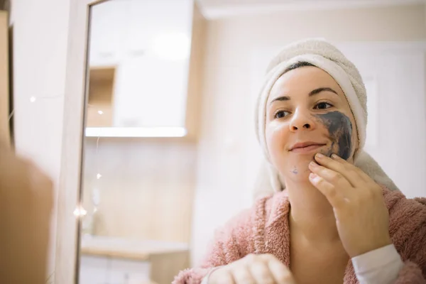 Mirrored image of a woman applying mud cream — Stock Photo, Image