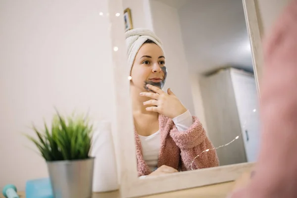 Chica aplicando máscara de carbón reflejado en el espejo — Foto de Stock