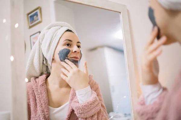 Reflejo de una chica frotando máscara de carbón en su cara — Foto de Stock