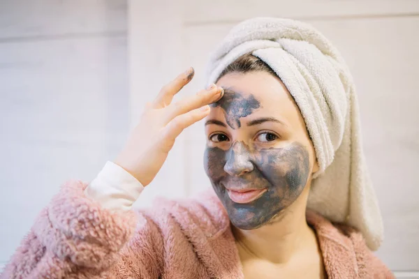 Chica sonriente aplicando crema de barro en la frente — Foto de Stock