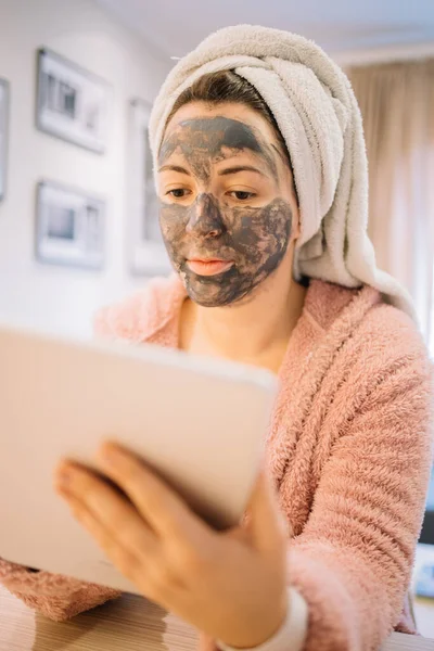 Mujer bonita con crema de barro sosteniendo una tableta — Foto de Stock