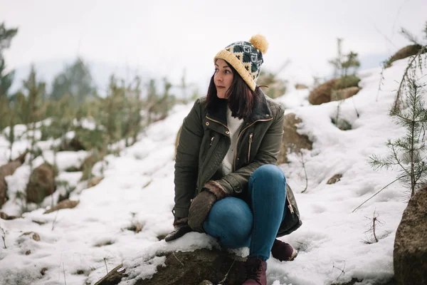 Woman sitting on rock in snowy forest — Zdjęcie stockowe