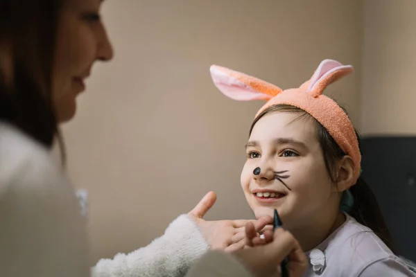 Lady with pen painting over little girls face