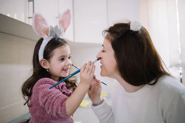 Adorable little girl painting mother face with brush