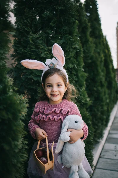 Cute toddler girl in bunny ears holding plush rabbit