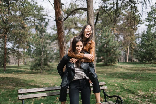 Улыбающаяся девушка, несущая свою сестру через парк — стоковое фото
