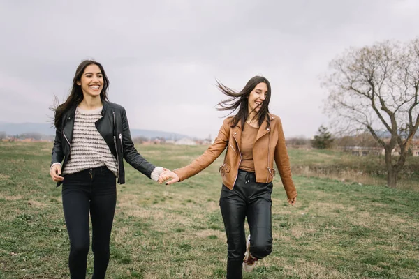Twin sisters holding hands and laughing outdoors