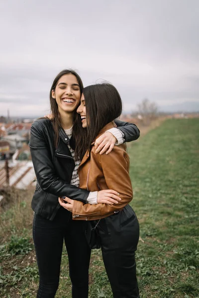 Две улыбающиеся девушки обнимаются, стоя на поле — стоковое фото