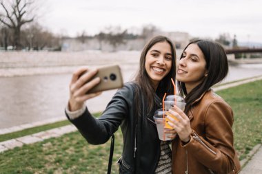 Kızlar nehir kenarında dururken selfie çekiyorlar.