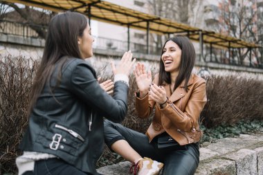 Arkadaşlar taş bariyerlerde otururken ellerle oynuyorlar