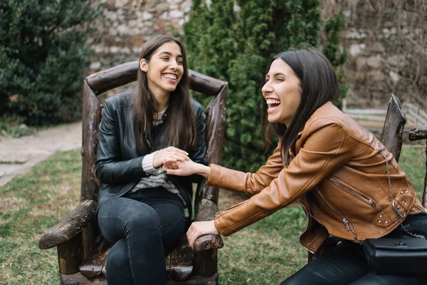 Siostry w drewnianych krzesłach trzymające się za ręce i śmiejące — Zdjęcie stockowe