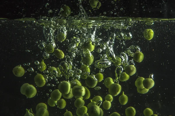 緑のエンドウ豆は黒い背景を持つ水に落ちる — ストック写真