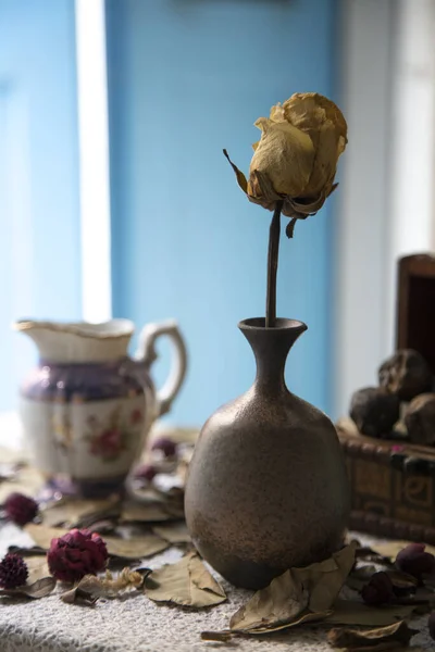Old vase with dried rose on table with dried leaves