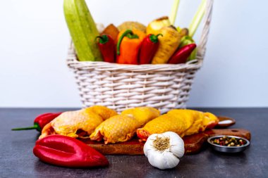 Sepet dolusu sebze ve kökle dolu. Tahtanın arkasında tavuk eti var.