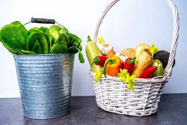 Groceries basket full of vegetables near bucket with spinach