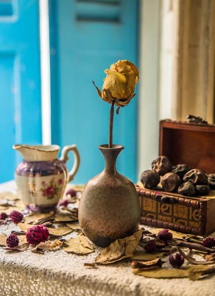 Dried yellow rose in antique vase with dried leaves