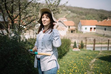 Bahçede elinde bahçe makası tutan bir kadın.