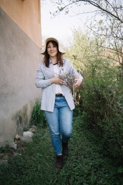 Elinde budanmış dallarla arka bahçede yürüyen kadın bahçıvan.