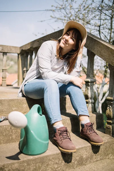 Счастливая девушка в шляпе сидит на лестнице с лейкой — стоковое фото