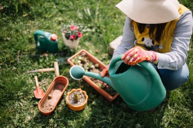 Bahçede çömelirken şapka sulayan bir kadın.
