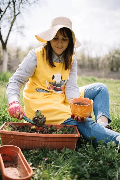 Wanita muda menanam bunga dan memegang tangan sekop dan pot — Stok Foto