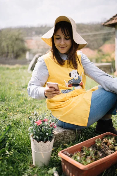 Perempuan tukang kebun mengenakan topi pemotretan tanaman dalam pot — Stok Foto