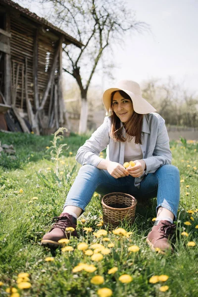 Wanita tersenyum duduk di padang rumput dengan dandelion — Stok Foto