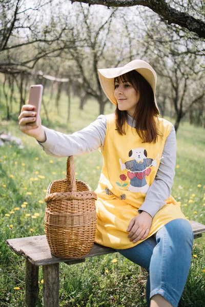 Happy woman sitting on bench with basket and taking selfie