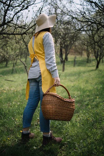 Tukang kebun perempuan dengan keranjang wicker berdiri di kebun — Stok Foto