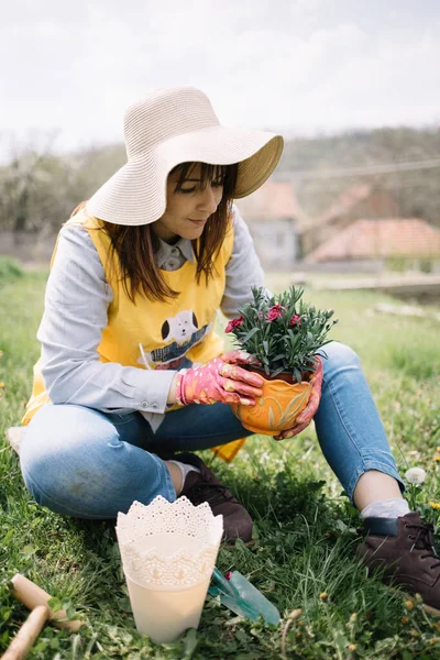 Gadis duduk di tanah dan memegang pot dengan bunga — Stok Foto