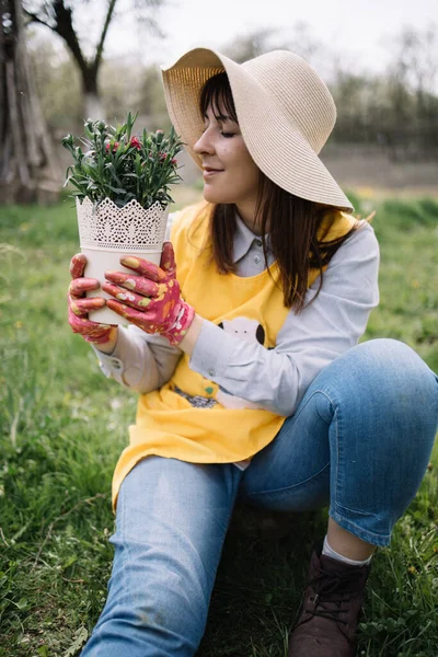 Tukang kebun wanita dengan sarung tangan berbau pot dengan bunga — Stok Foto