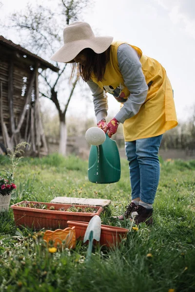 Lady dengan topi dan sarung tangan memegang air bisa lebih dari pot — Stok Foto
