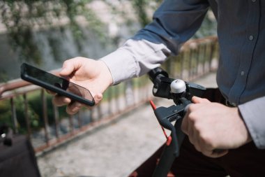 Adam elektrikli scooter dümeni tutarken telefonu kullanıyor.