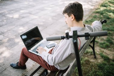 Elektrikli scooter 'ın yanındaki dizüstü bilgisayarda çalışan adamın arka planı