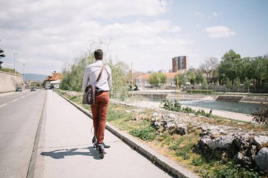 Nehir kenarındaki yolda elektrikli scooter kullanan bir adam.